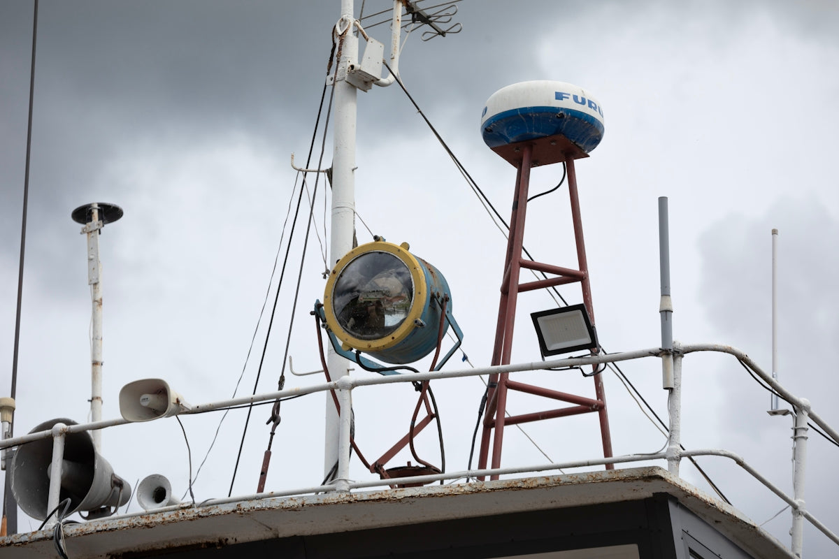 A boat's mast with a spotlight, radar dome, and antennas.